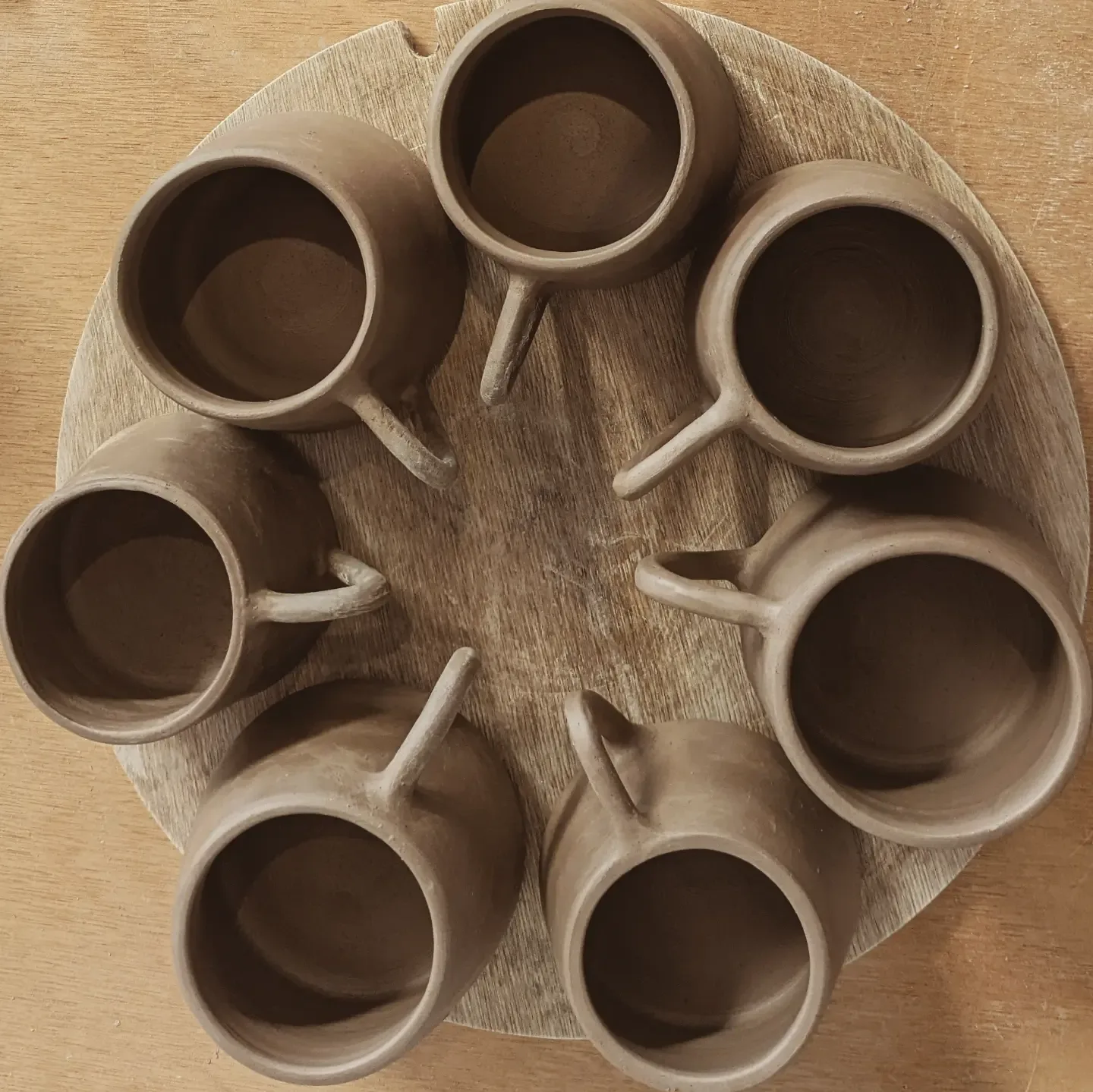 Unfired stoneware mugs arranged on a wooden board in the studio