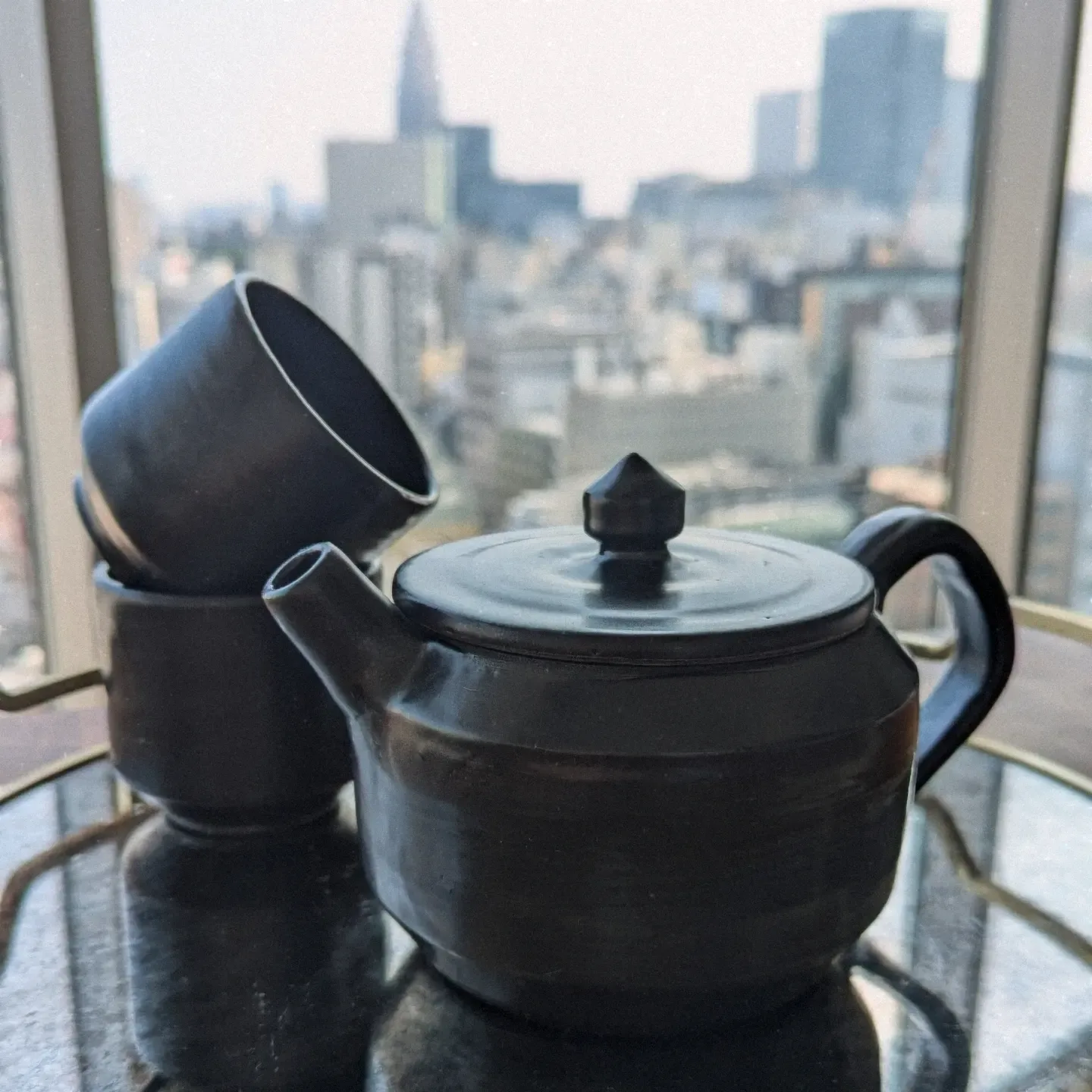 Matte black teapot and stacked cups by a window