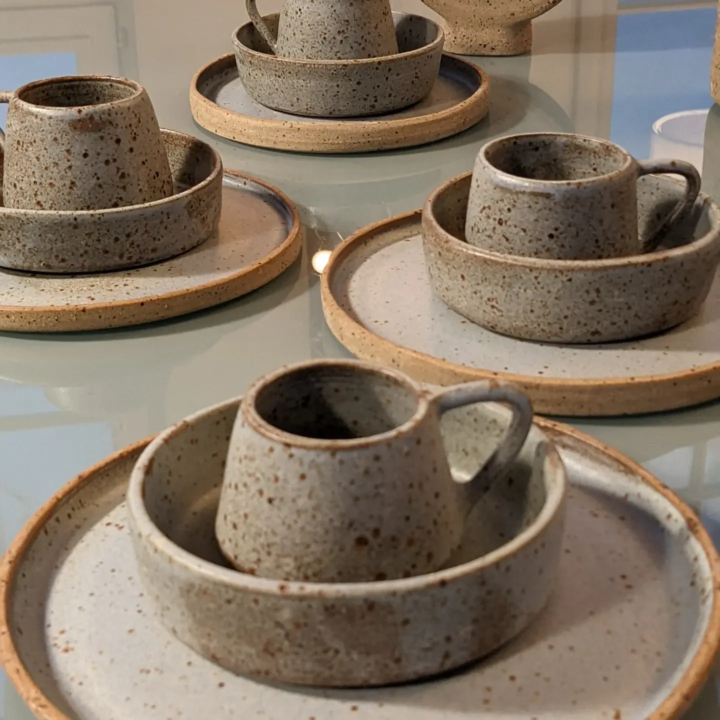 Place settings of speckled stoneware mugs, bowls and plates
